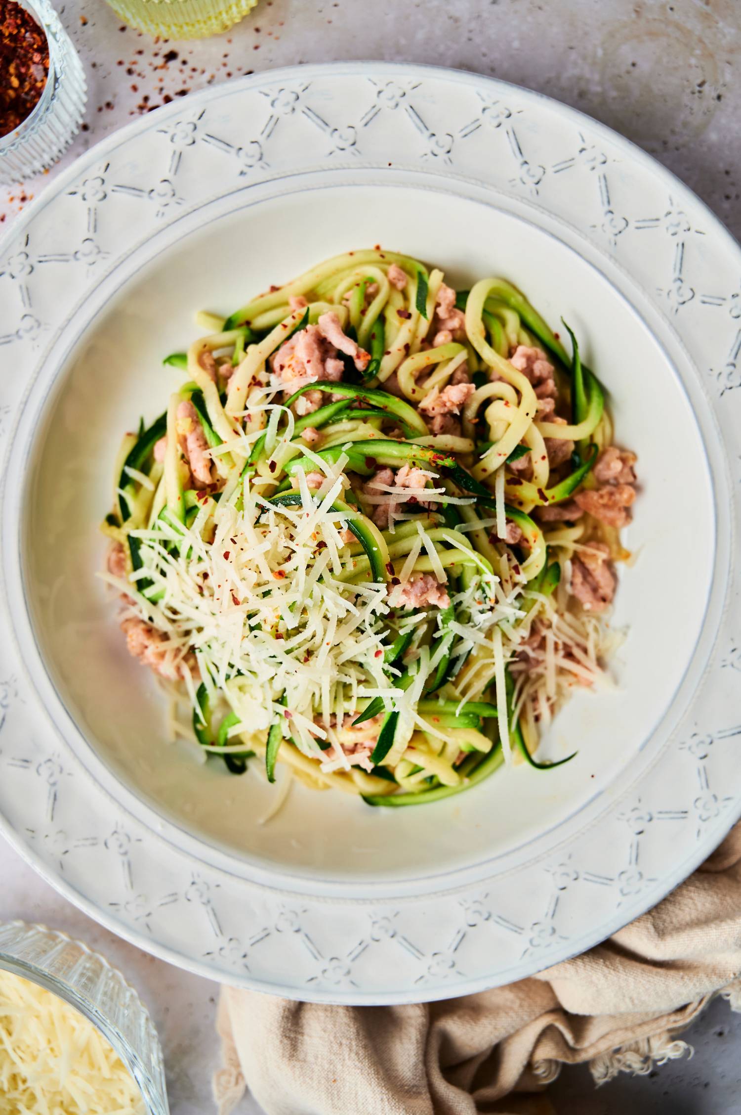 Sausage zoodles with Parmesan cheese and red pepper flakes in a bowl.