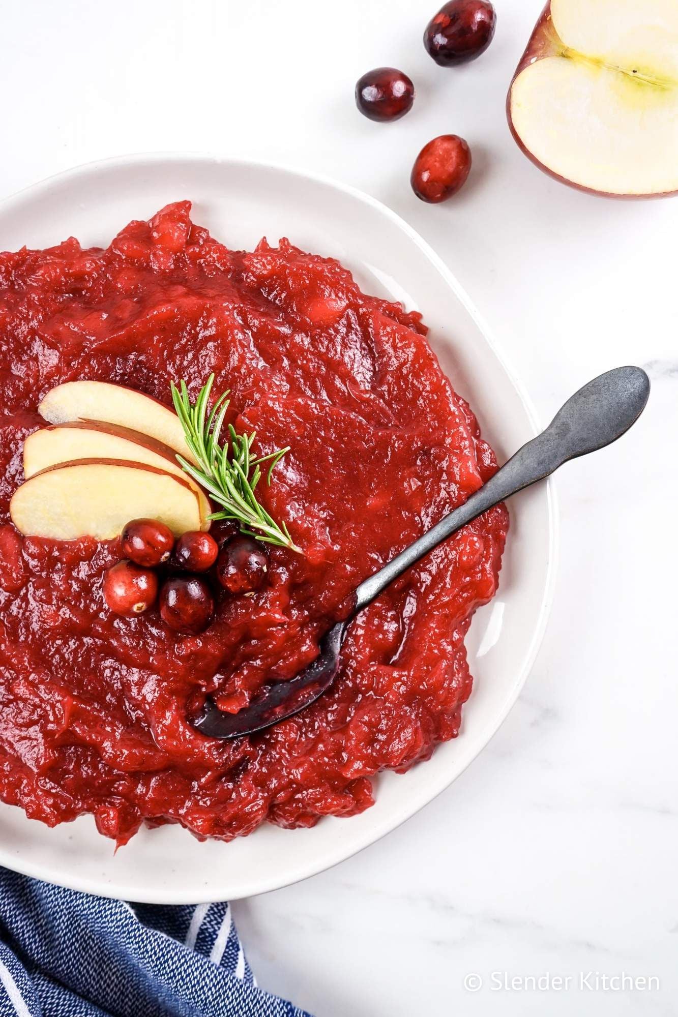 Cranberry apple sauce in a bowl with sliced apples and fresh cranberries with a blue napkin.