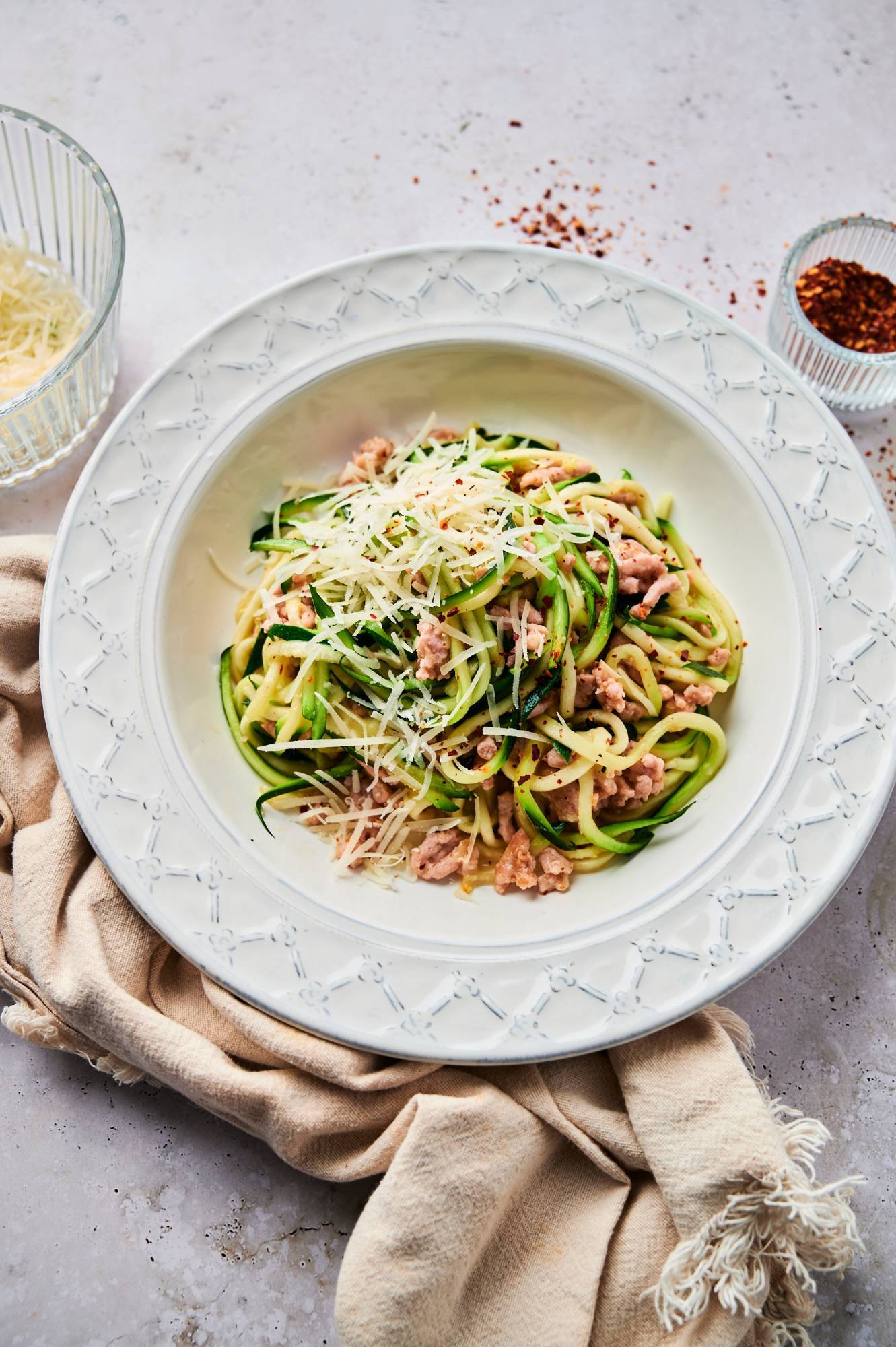 Sausage and zucchini noodles served with Parmesan cheese in a bowl with red pepper flakes.
