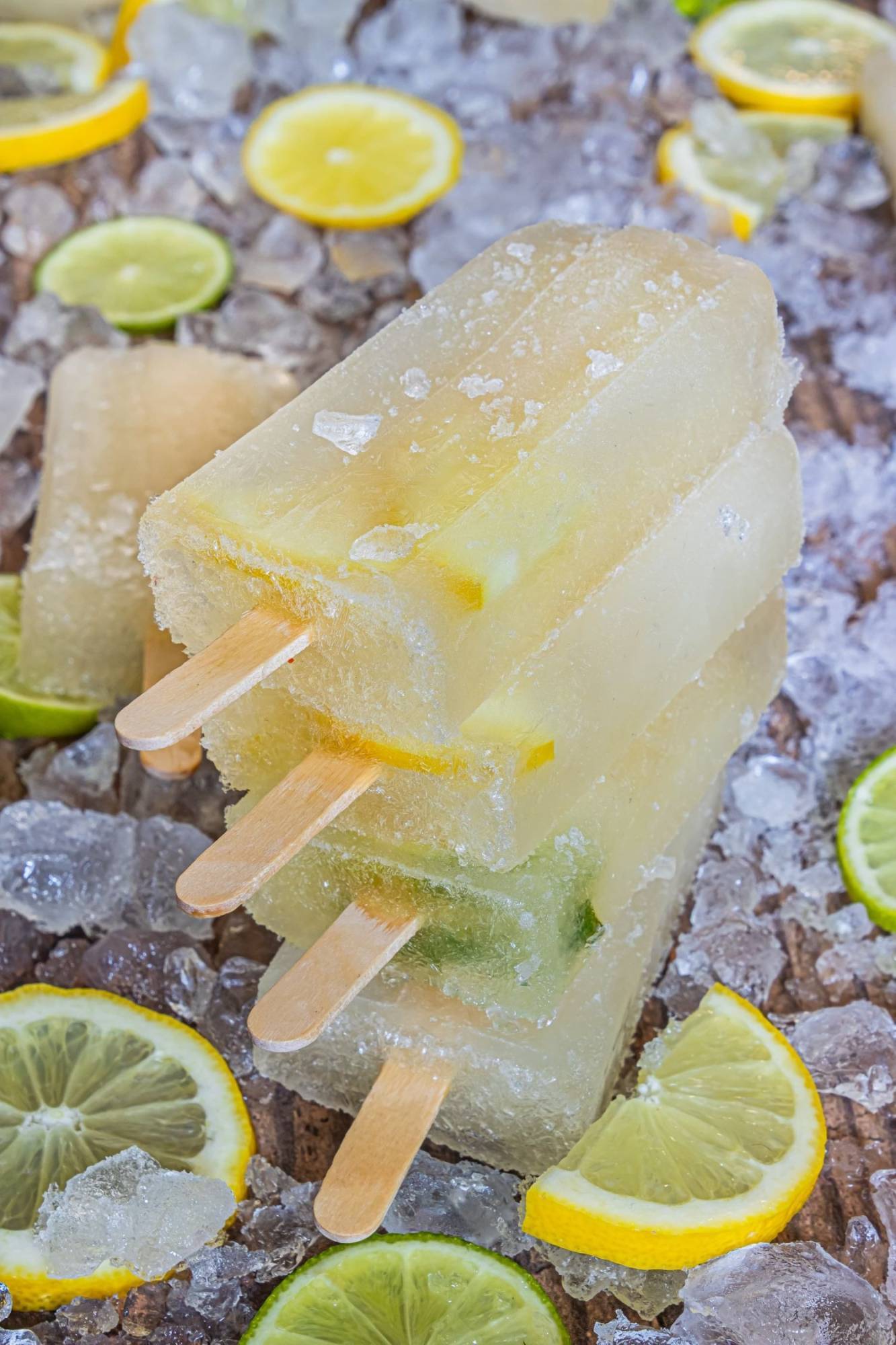 Three frozen lemon-lime popsicles stacked on ice, surrounded by fresh lemon and lime slices.