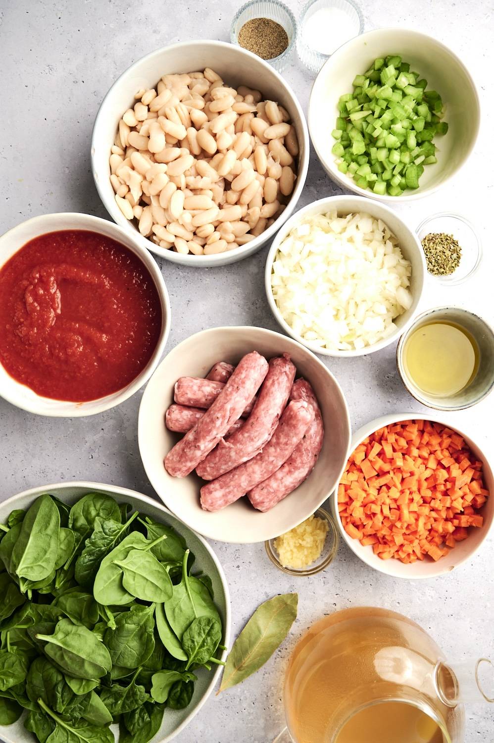 Ingredients for sausage, white bean, and spinach soup including ground sausage, white beans, carrots, celery, onion, garlic, tomato sauce, spinach, and chicken broth.