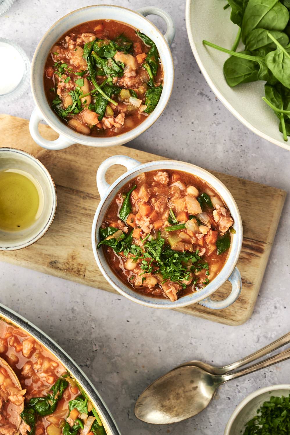 Sausage and white bean soup with spinach served in tow bowls with fresh parsley.