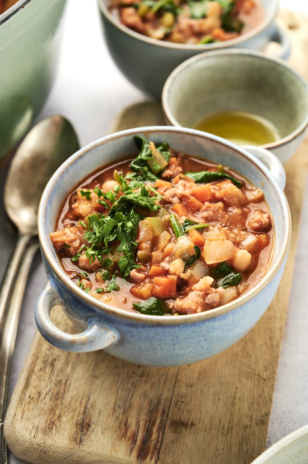 White bean, sausage, and spinach soup in a bowl with tomato broth and fresh parsley..