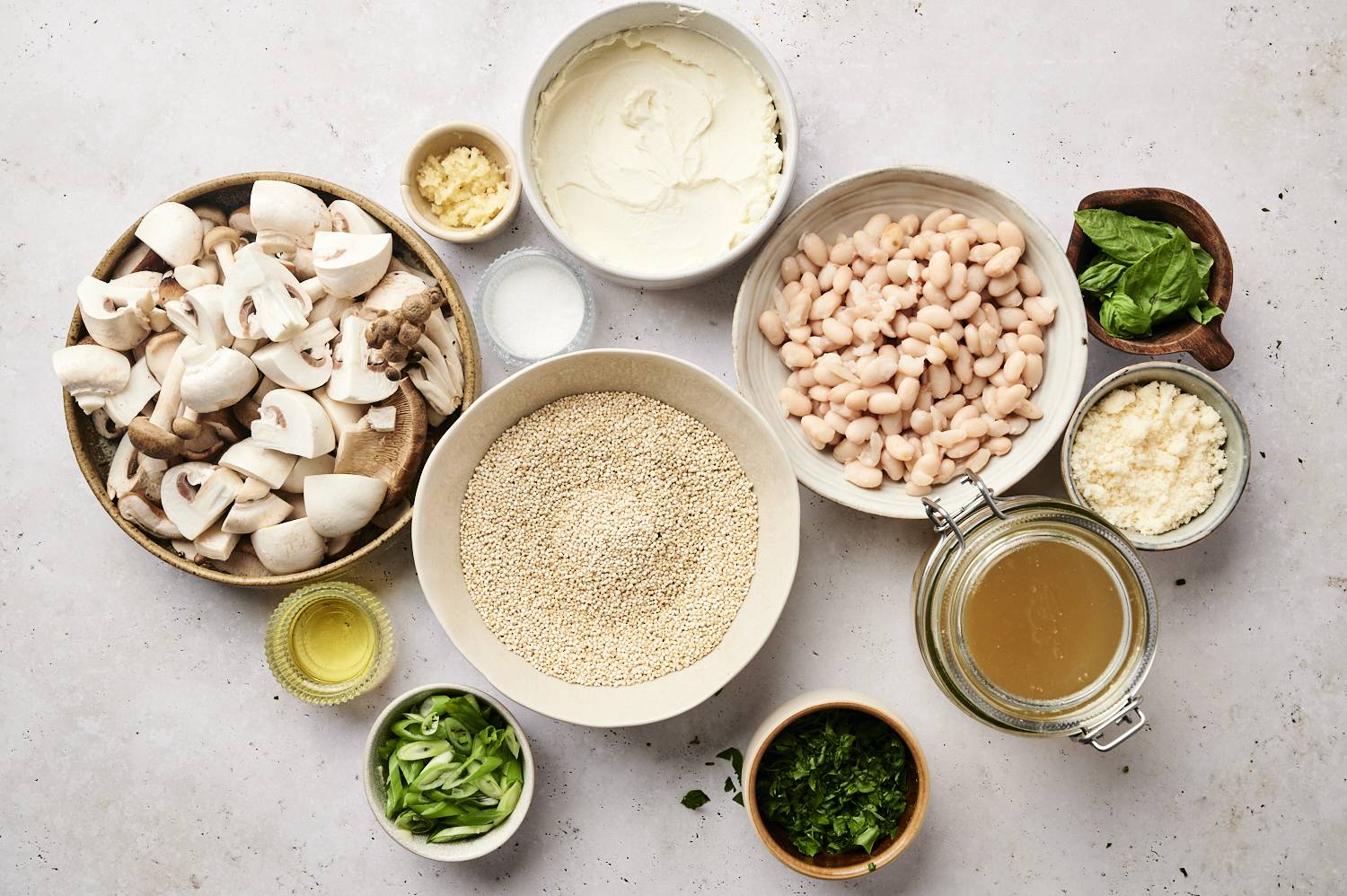 A top-down view of ingredients for slow cooker garlic mushroom quinoa, including chopped mushrooms, quinoa, white beans, broth, and seasonings.