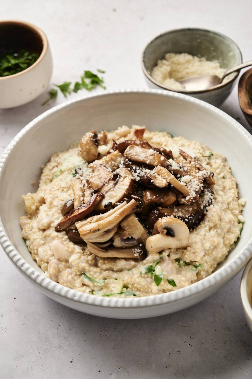 Creamy quinoa with sautéed mushrooms, spinach, and Parmesan, served in a white bowl with a warm, rustic backdrop.