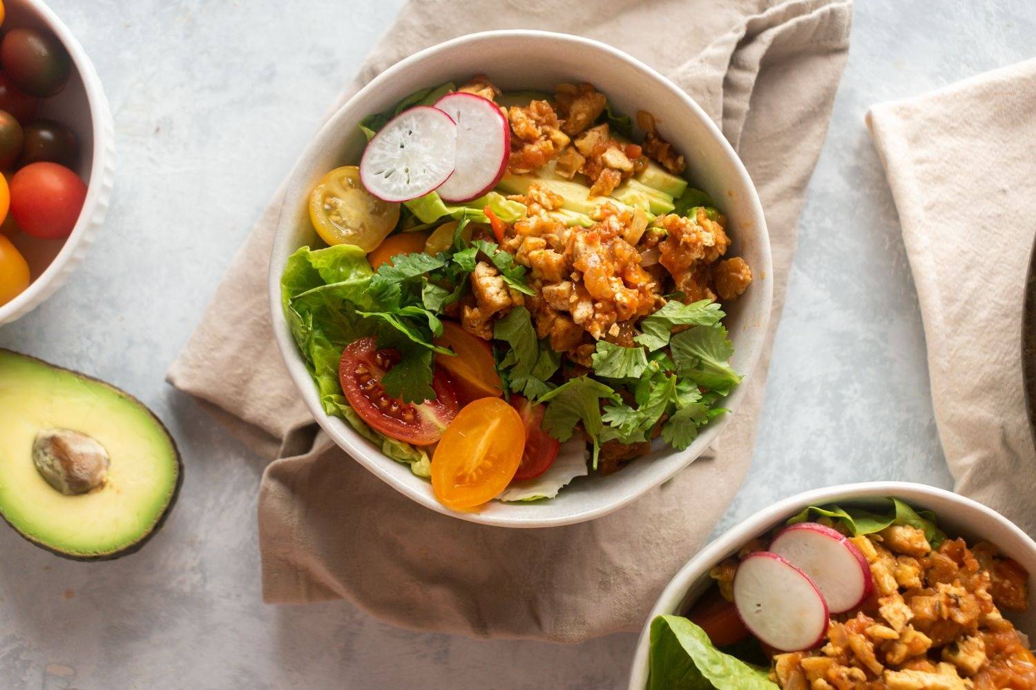 Homemade Sofritas made with tofu, chipotle peppers, and tomato sauce in a two bowls with lettuce, avocado, and cilantro.