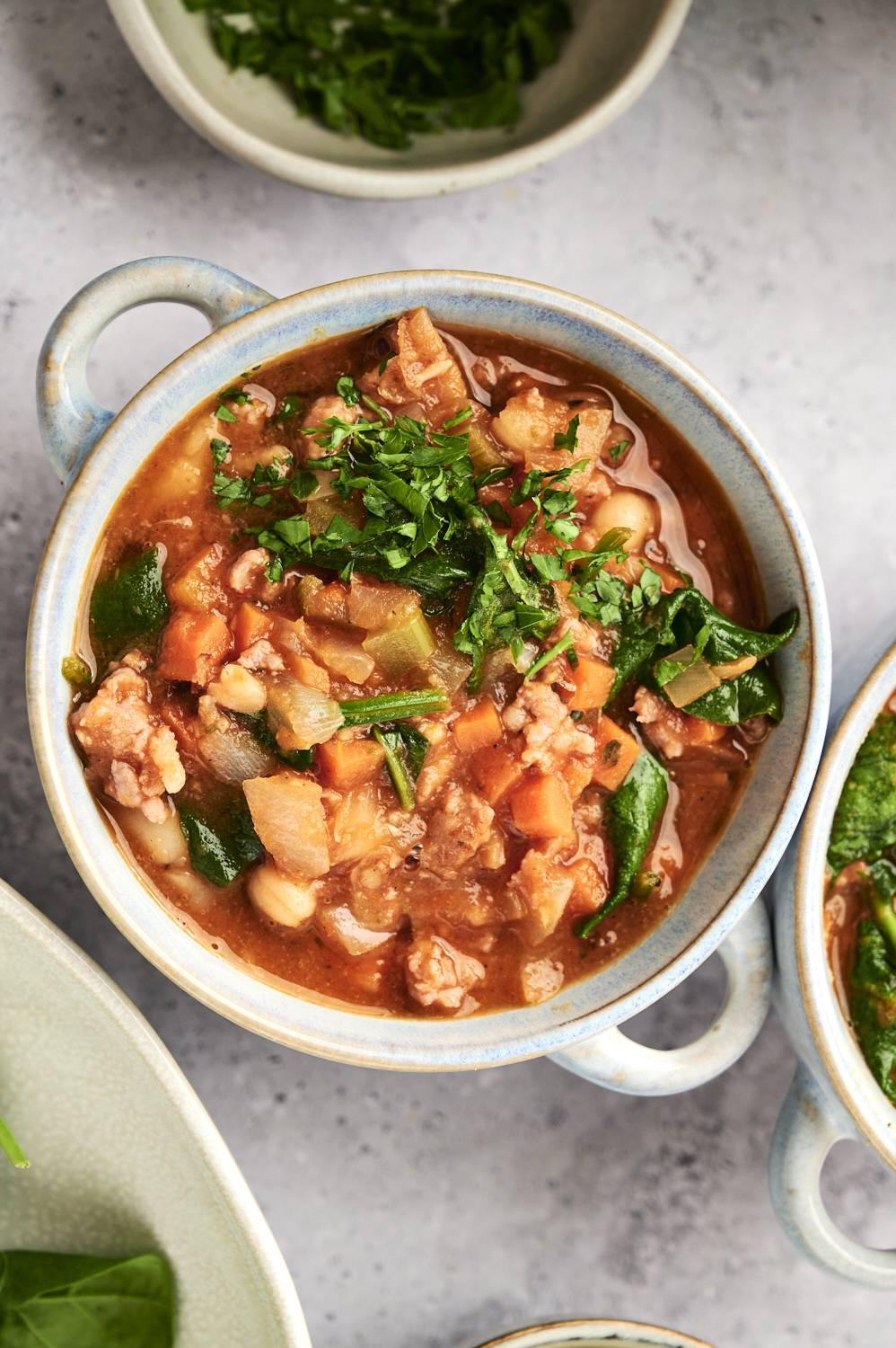 Sausage and bean soup with spinach, carrots, onions, celery, and garlic served in a bowl.