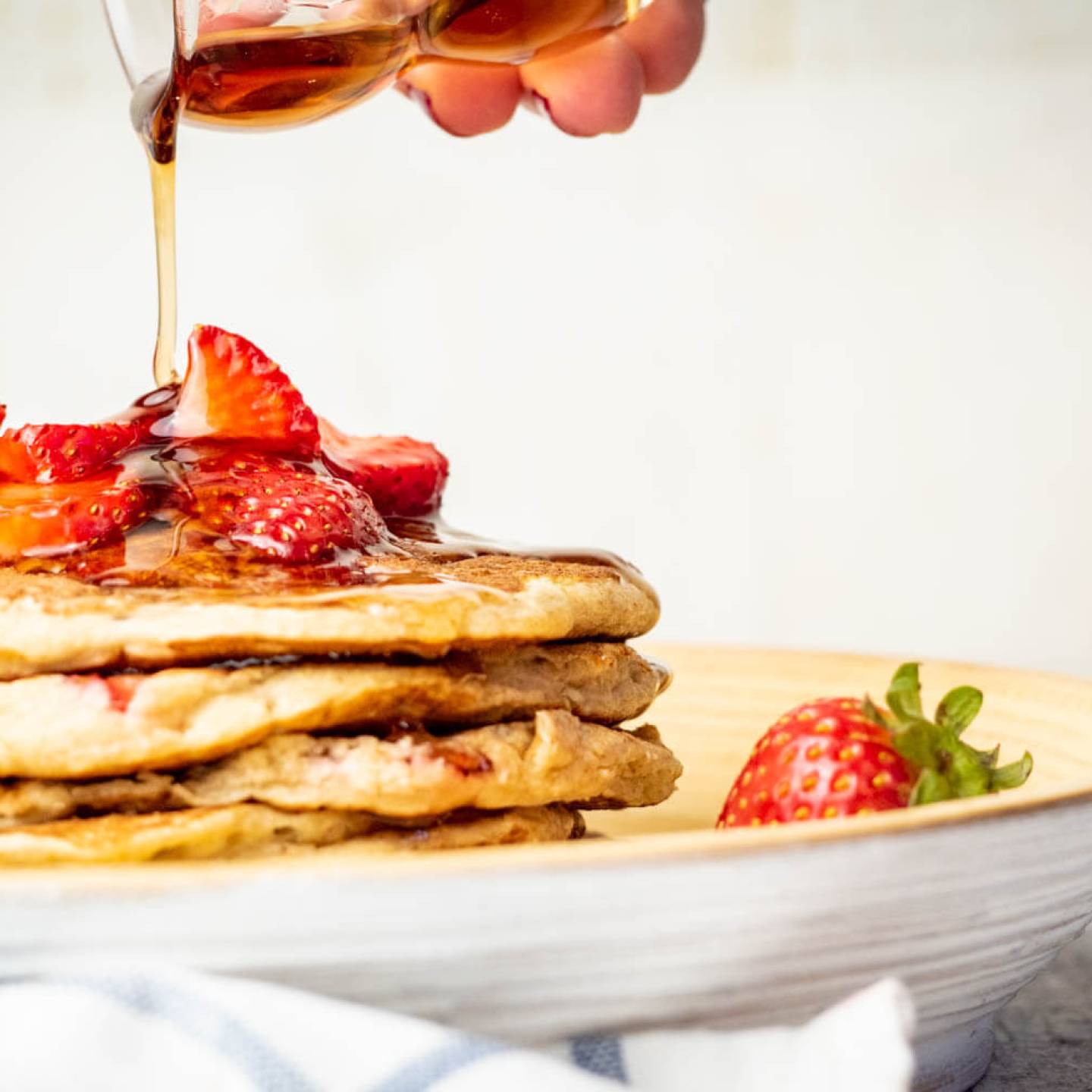 Strawberry Banana Oat Pancakes with maple syrup being poured on top.