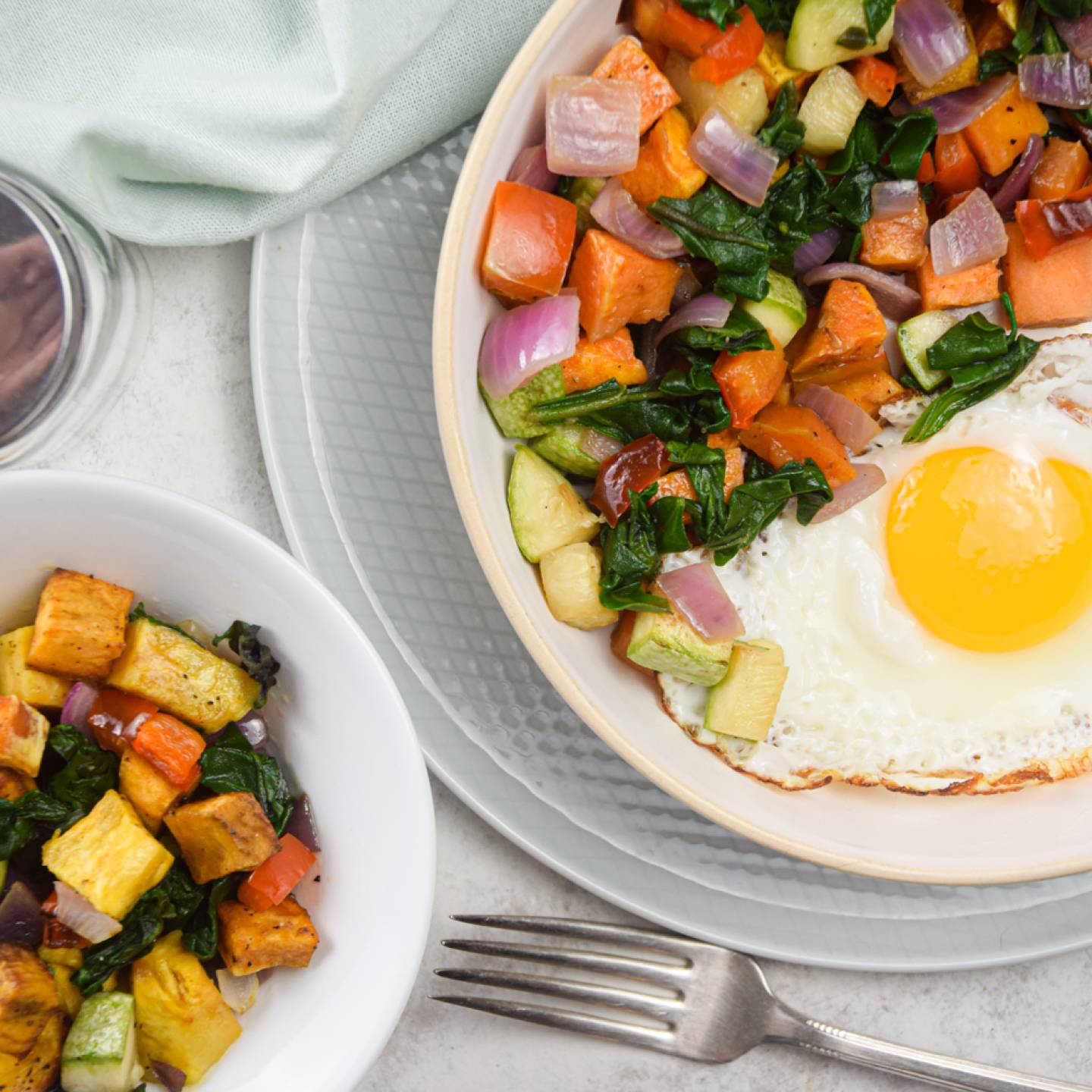 Sweet potato hash with sweet potatoes, zucchini, onions, peppers, and a fried egg on a plate with sliced sausage.