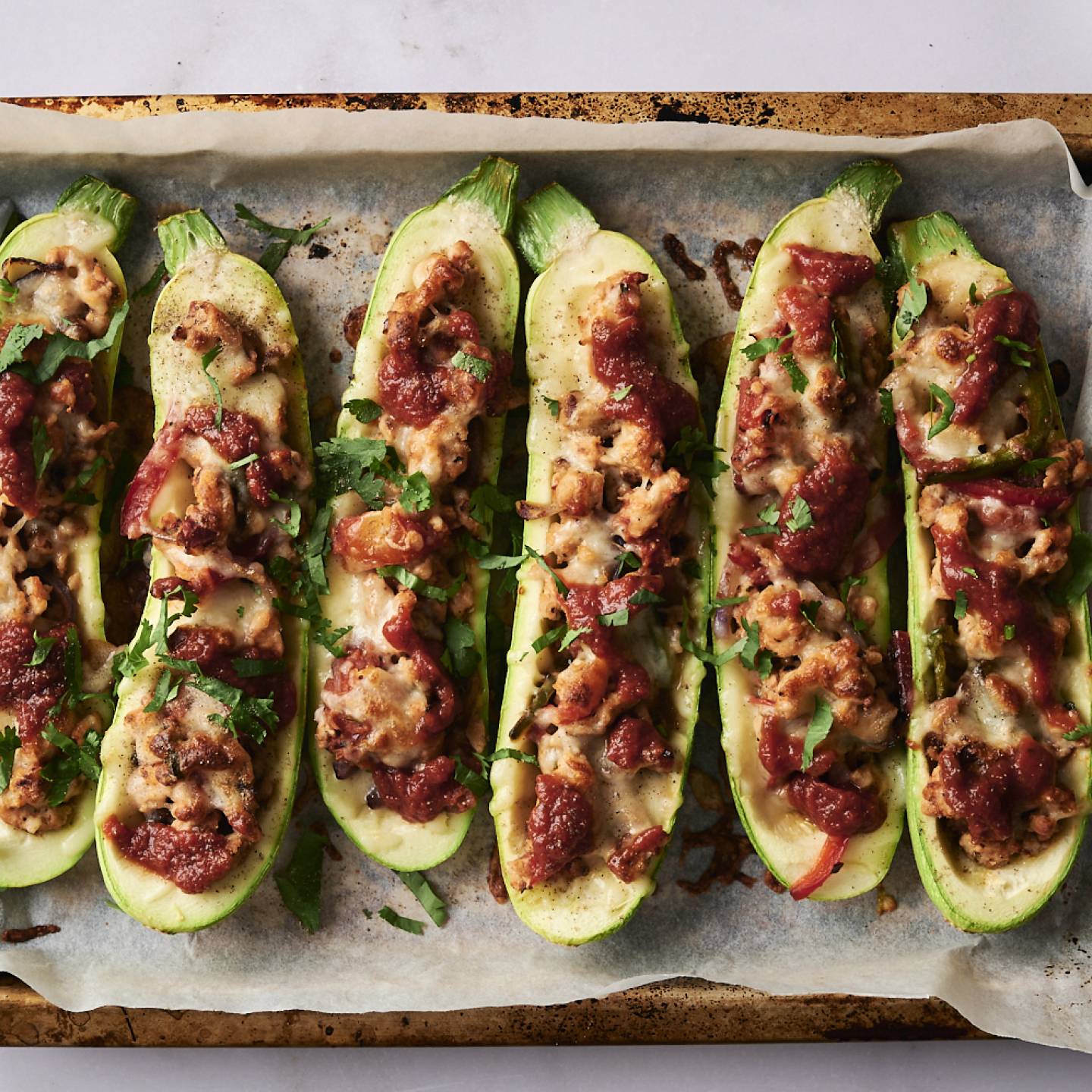 Baked Tex-Mex stuffed zucchini with cheese, tomato sauce, and cilantro on a parchment-lined baking tray.