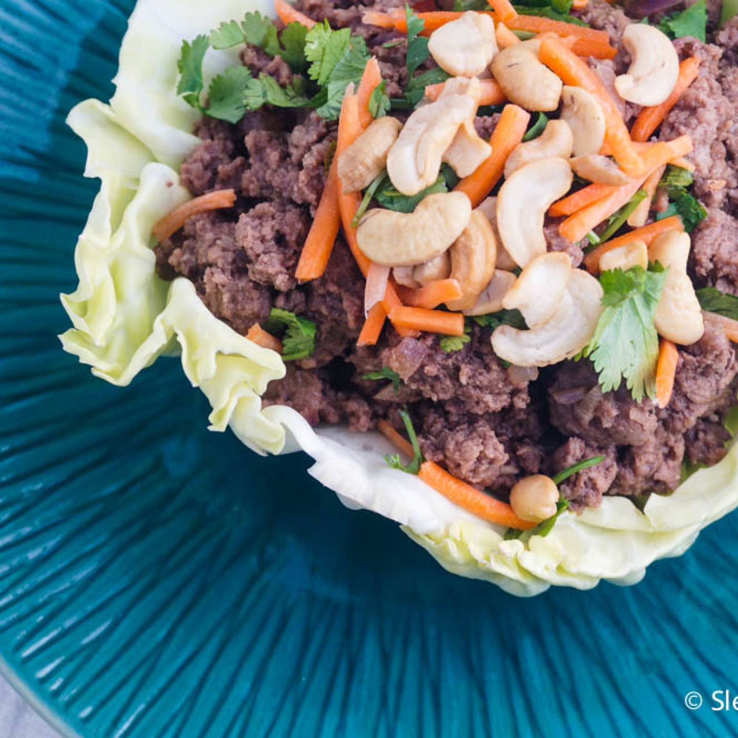 Thai beef cabbage wraps with cashews, cilantro, and carrots on a plate. 