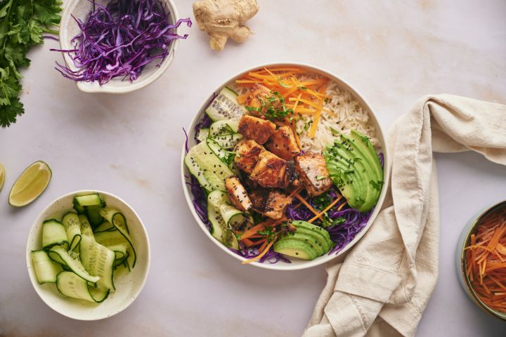 Asian salmon rice bowls with crispy salmon pieces served with rice, purple cabbage, edamame, carrots, and cucumber.