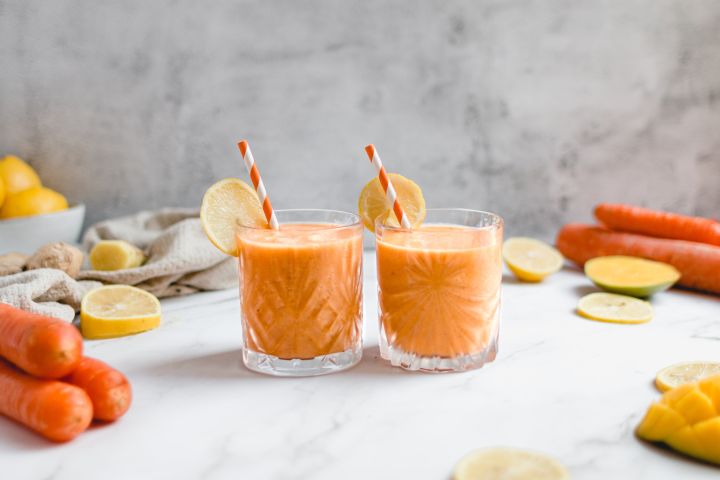 Carrot ginger smoothie with shredded carrots, banana, and mango in two glasses with straws.