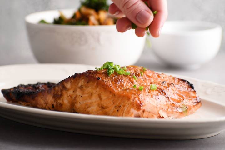 Crispy baked brown sugar salmon on a plate with chives being sprinkled on top.