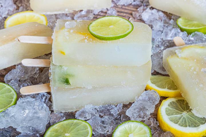 Homemade lemon lime popsicles with slices of lime on a plate with ice.