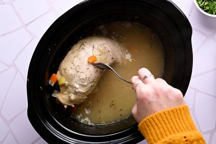 Cooked turkey being removed from a slow cooker.