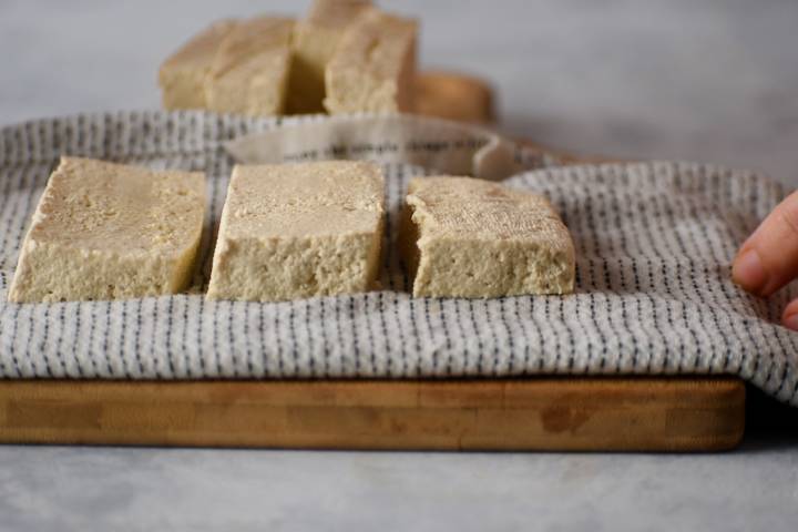 Tofu being pressed on kitchen towels to remove moisture.