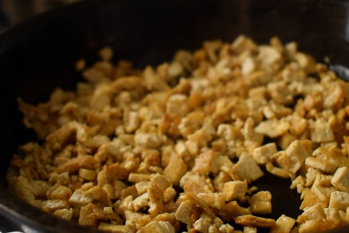 Small tofu chunks cooking in a skillet with oil.