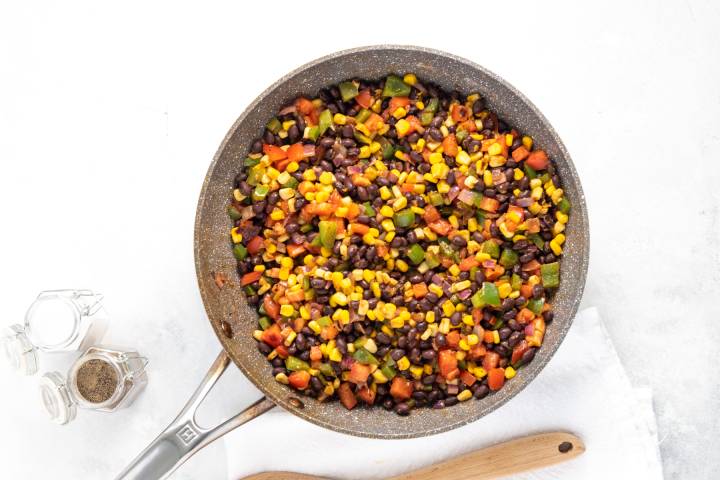 Black beans, peppers, red onions, corn, tomatoes, and taco seasoning in a skillet.