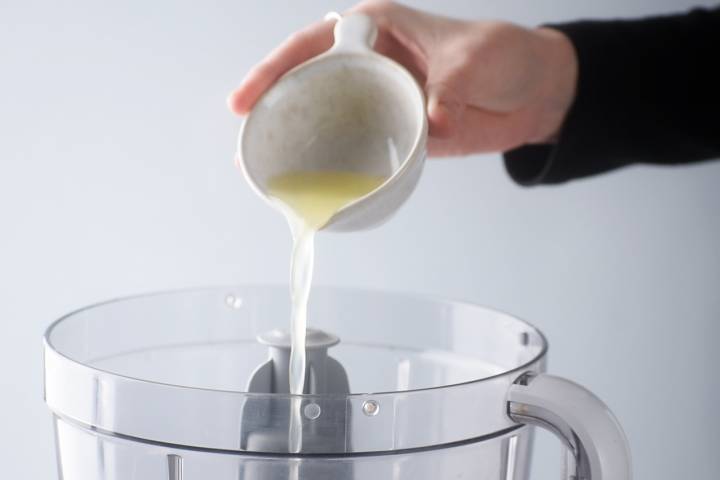 Lemon juice being poured into a food processor for white bean hummus.