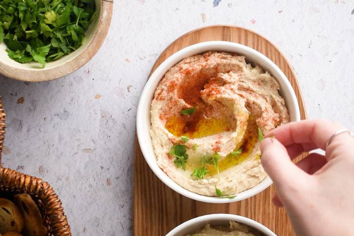 Fresh herbs being added to hummus with white beans in a bowl.