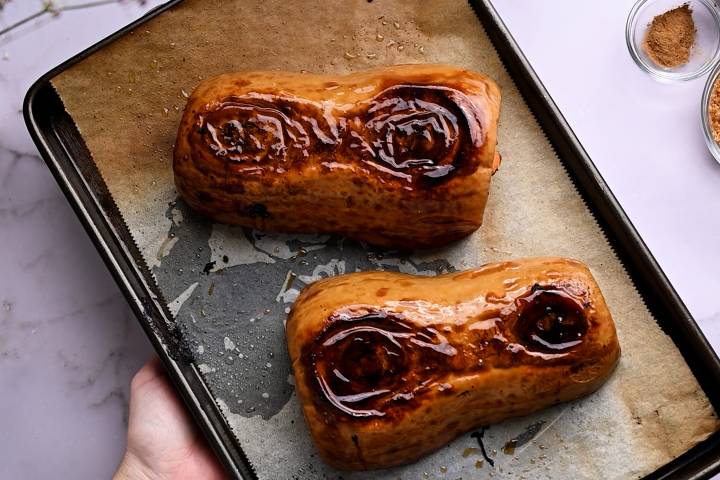 Roasted butternut squash halves with browned edges on a baking sheet.