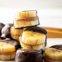 Stacked banana slices filled with peanut butter, dipped in dark chocolate, arranged artfully on a light background.