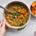Slow cooker lentil soup with lentils, squash, carrots, spinach, and potatoes in a bowl with a hand holding it.