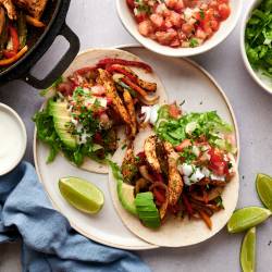 Fajita tacos with chicken breast, peppers, onions, sour cream, avocado, and salsa in corn tortillas.