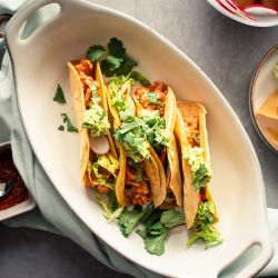 Ground turkey tacos in crispy baked tortillas with salsa, lettuce, radishes, and guacamole on a plate.