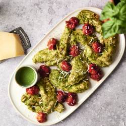 Juicy pesto chicken tenders topped with roasted cherry tomatoes and Parmesan cheese, served with extra pesto sauce on the side.