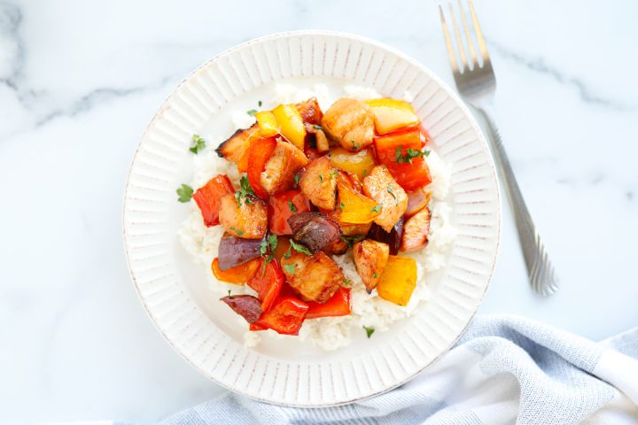 Sheet pan honey Sriracha chicken and vegetables on a white plate with rice.