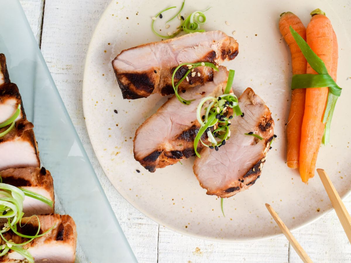 Asian grilled pork tenderloin on a plate with carrots, green onions, and chopsticks.