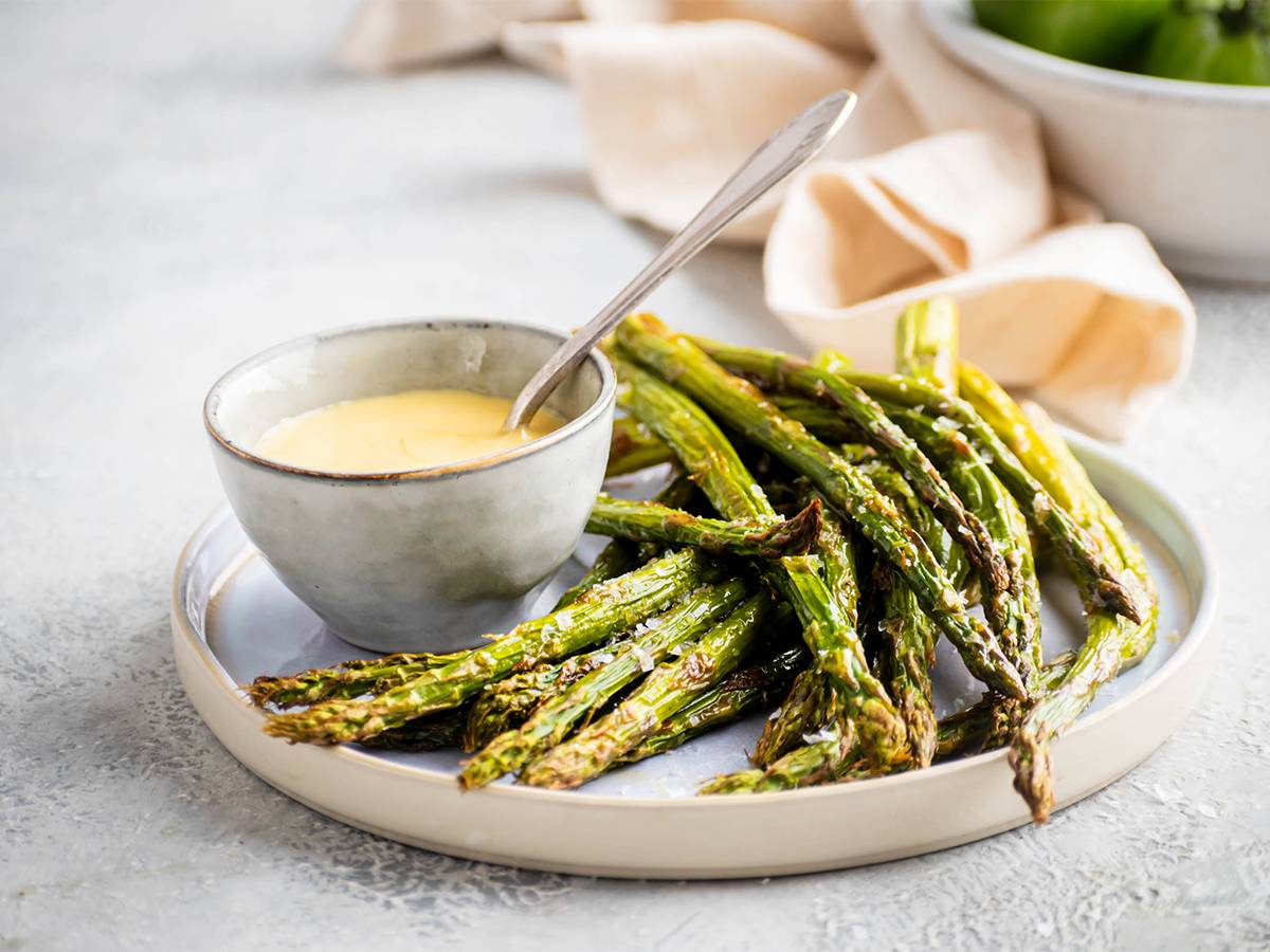 Roasted asparagus with olive oil, salt, and pepper served on a plate with hollandaise sauce.