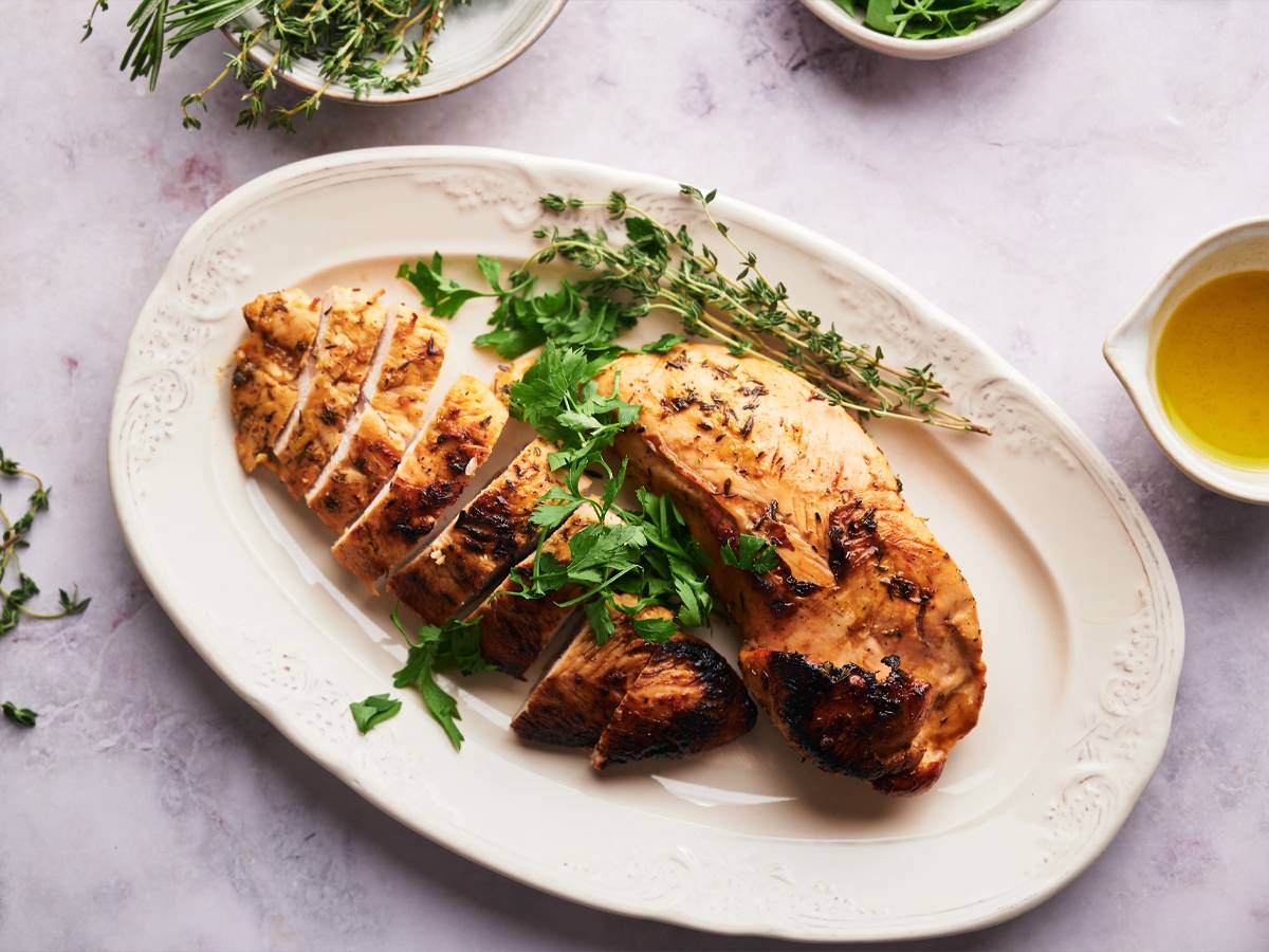 Baked turkey tenderloin sliced on a plate with fresh herbs.